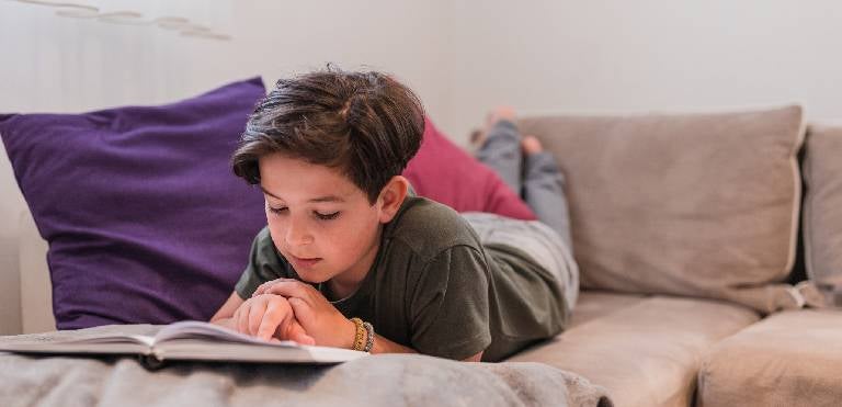 Un niño haciendo ejercicios de comprensión lectora acostado